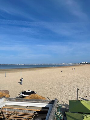 A beach with a clear sky, a sandy shore, and a few people. There are umbrellas and a wooden structure in the foreground. - Baie de La Baule - Centre ville à 30 mètres de la mer et du port de plaisance (Pornichet)