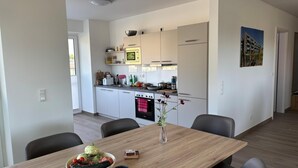 Ett modernt kök med vita skåp, en inbyggd ugn och en matplats med ett träbord och stolar.