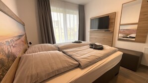 Ett hotellrum med en stor säng, en platt-TV som är monterad på väggen och en tavla på väggen.
