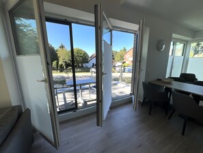 A modern kitchen with a large window, a dining area with a table and chairs, and a sliding glass door leading to an outdoor patio. - Hello and welcome to Apartment Heimersdorf! (Nordseebad Dangast)