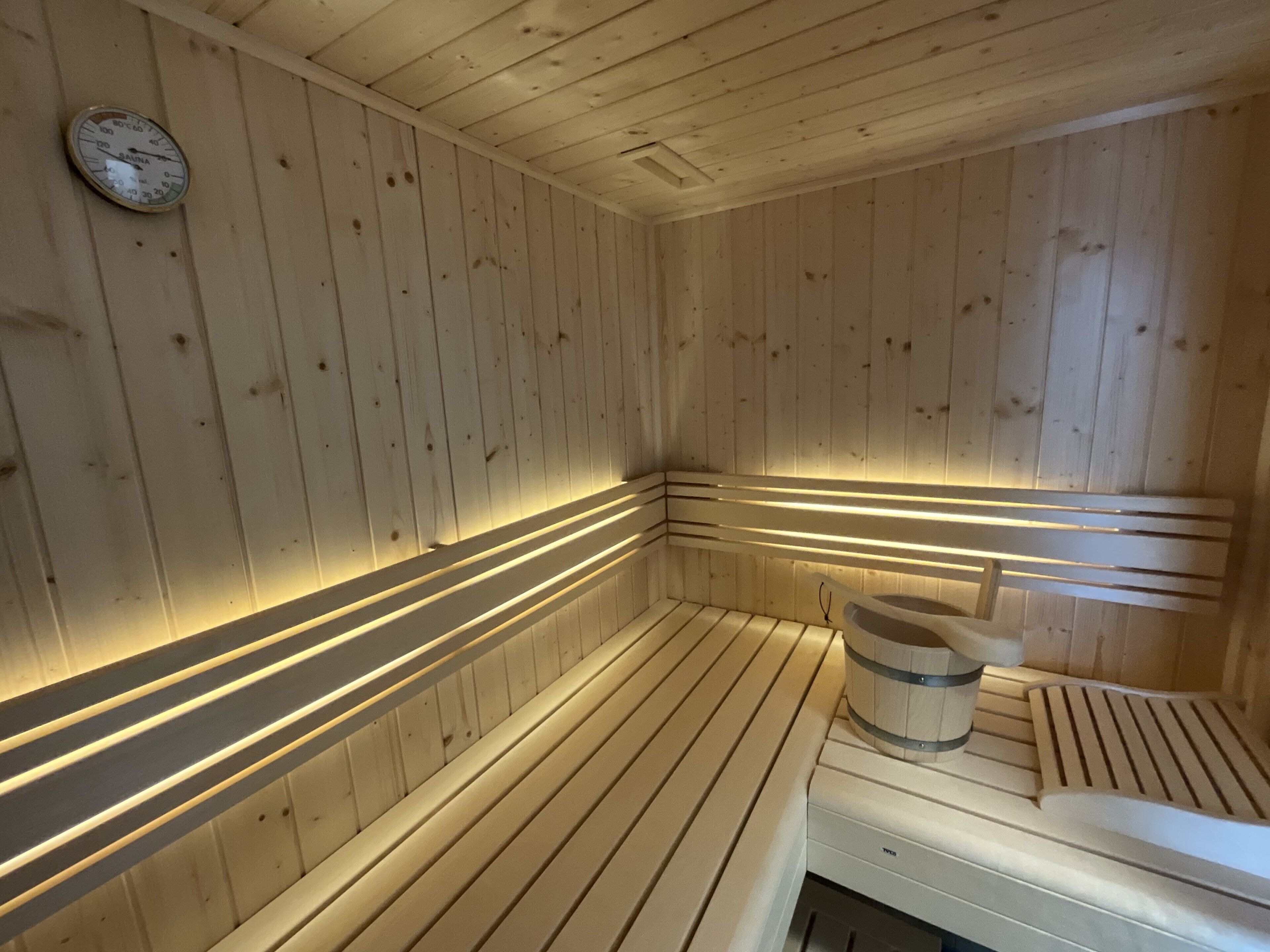 Eine Sauna mit Holzwänden und -bänken, einem sichtbaren Temperaturanzeiger und einem Eimer.