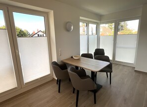 A dining area with a table and chairs, large windows, and a view of the neighborhood. - Hello and welcome to Apartment Rodenkirchen! (Nordseebad Dangast)