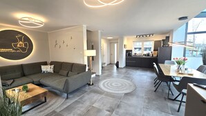 A modern living room with a sectional sofa, a coffee table, and a dining area with a table and chairs. - Moin and welcome to the vacation home "achtern diek" (Dangast)