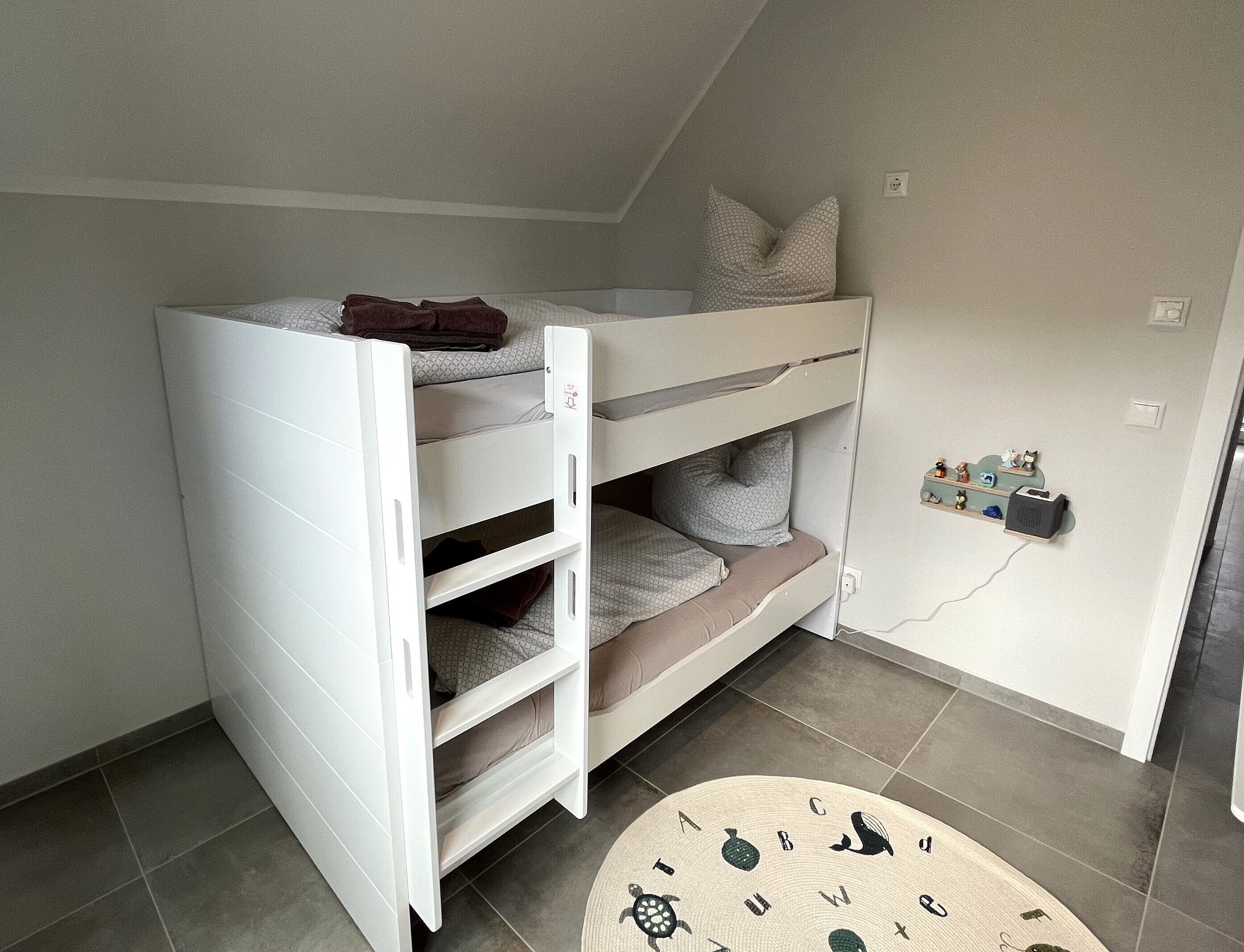 A bunk bed with a desk drawer, a small shelf with figurines, and a round table with a letter pattern.