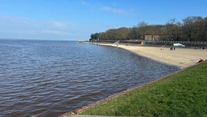 A coastal beach with a grassy area, a wooden fence, and a building with a brick facade. - Moin and welcome to the vacation home "achtern diek" (Dangast)
