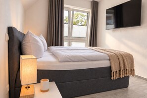 Ein modernes Schlafzimmer mit einem Bett, einer Nachttischlampe und einem an der Wand montierten Fernseher.