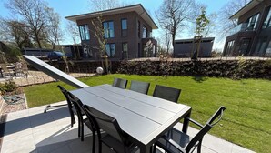 Eine Terrasse mit Tisch und Stühlen, ein kleiner Garten und moderne Häuser im Hintergrund.