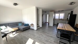 Ein zeitgemäßer Wohnraum mit einem grauen Sofa, einem kleinen runden Tisch und einem Esstisch mit Stühlen.