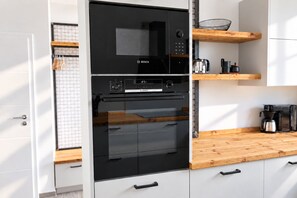 A kitchen with a Bosch oven and microwave, wooden shelves, and a coffee maker. - Hello and welcome to the Ackerpulko Vacation Home! (Dangast)