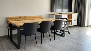 Ein modernes Wohnzimmer mit einem Holzesstisch, zwei schwarzen Stühlen, einem an der Wand befestigten Flachbildfernseher und einer eingebauten weißen Kommode.