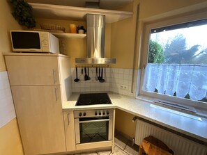 A kitchen with a stove, oven, microwave, and hanging utensils. - Hello and welcome to the Friesenkoje! (Dangast)