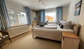 Makuuhuone, jossa on sänky, puinen yöpöytä, tuoli ja ikkuna, jossa on verhot.