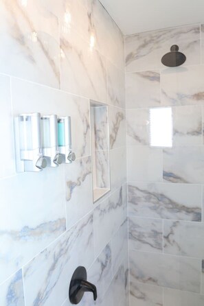 Une salle de bain moderne avec des carreaux de marbre, une pomme de douche et un sèche-mains.