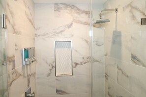 Un baño moderno con baldosas de mármol, una ducha y dispensador de jabón para manos.