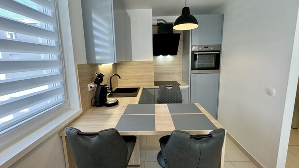 A compact kitchen with a dining table, chairs, a coffee machine, and a built-in oven. - Coastal Family Apartment in Zadar (Zadar)