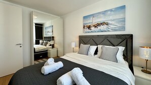 A modern hotel room with a large bed, a painting of a lighthouse, and a mirror reflecting the room. - Coastal Family Apartment in Zadar (Zadar)