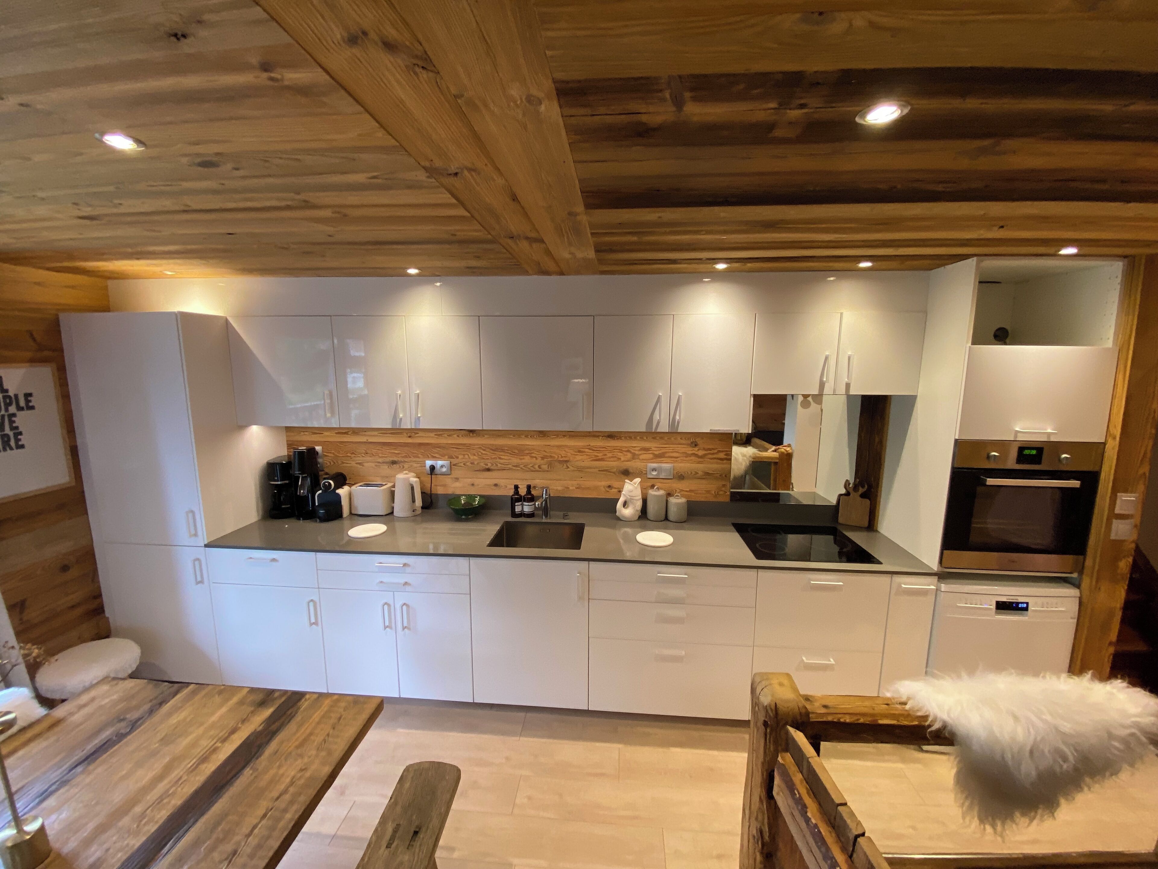 Une cuisine moderne avec des armoires blanches, un plafond en bois et un four encastré.