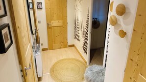 A hallway with wooden flooring, a round woven rug, a fluffy stool, and a wooden door with a mirror and picture frames on the wall. - Luxury apartment at the foot of the slopes- (Arâches-la-Frasse)