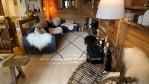 A cozy living room with a large sofa, a wicker chair, and a wooden wall. - Luxury apartment at the foot of the slopes- (Arâches-la-Frasse)