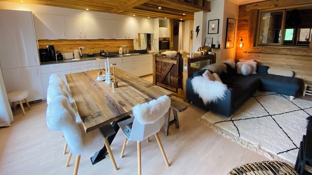 A modern kitchen with wooden accents, a dining area with a wooden table and white chairs, and a cozy living area with a blue sofa and white furry cushions. - Luxury apartment at the foot of the slopes- (Arâches-la-Frasse)