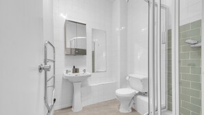 Een moderne badkamer met een douchecabine van glas, een wastafel op een zuil en een toilet.