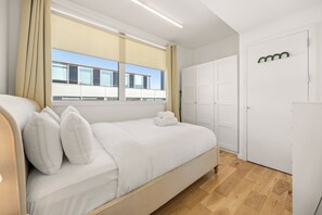 A modern hotel room with a bed, a window with curtains, a wardrobe, and a wooden floor. - Spacious Fitzrovia Apt with Central A/C (London)