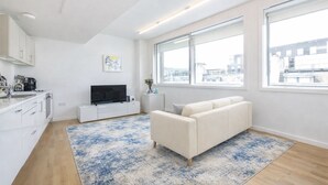 Een modern appartement met keuken, een woongedeelte met bank en televisie, grote ramen en uitzicht op de stad.