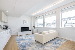 Ein modernes Apartment mit Küche, einem Wohnbereich inklusive Sofa und Fernseher, großen Fenstern und Blick auf die Stadt.