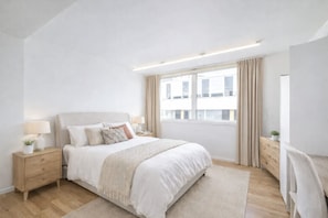 Ein modernes Schlafzimmer mit einem großen Bett, Nachttischen, einem Fenster mit Vorhängen und Blick auf Gebäude.