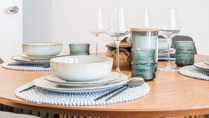 Een eettafel gedekt met glazen, kommen en borden, met een modern kunstwerk erboven.