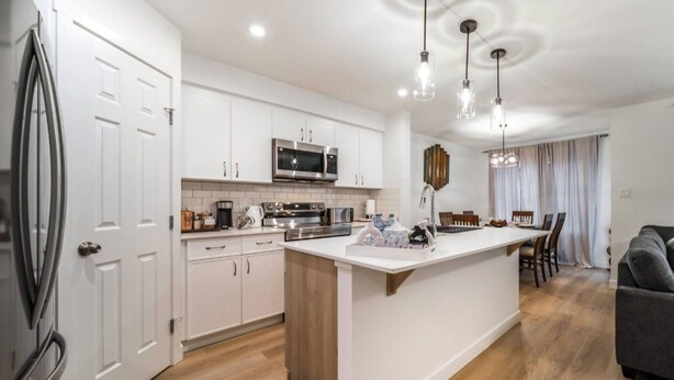 A modern kitchen with white cabinets, stainless steel appliances, and a central island. - Chiccityescape3bdrm King (Stony Plain)