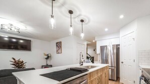 A modern kitchen with a central island, stainless steel appliances, and pendant lighting. - Chiccityescape3bdrm King (Stony Plain)