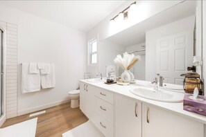 Een moderne badkamer met een wit wastafelmeubel en een grote spiegel. Handdoeken hangen aan de muur en er is een douchehoek zichtbaar.