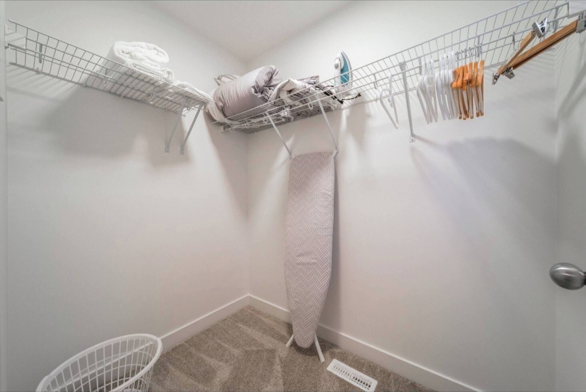 A laundry area with a drying rack, a hanging iron, and a storage shelf.
