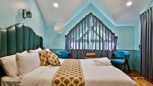 Una habitación de hotel con cama, escritorio, silla, ventilador y cortinas.
