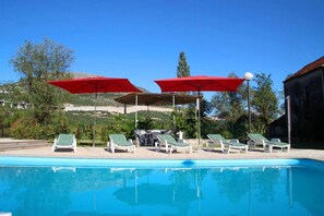 A swimming pool with lounge chairs and red umbrellas. - 14-guest Holiday Home in Vrgorac (Vrgorac)