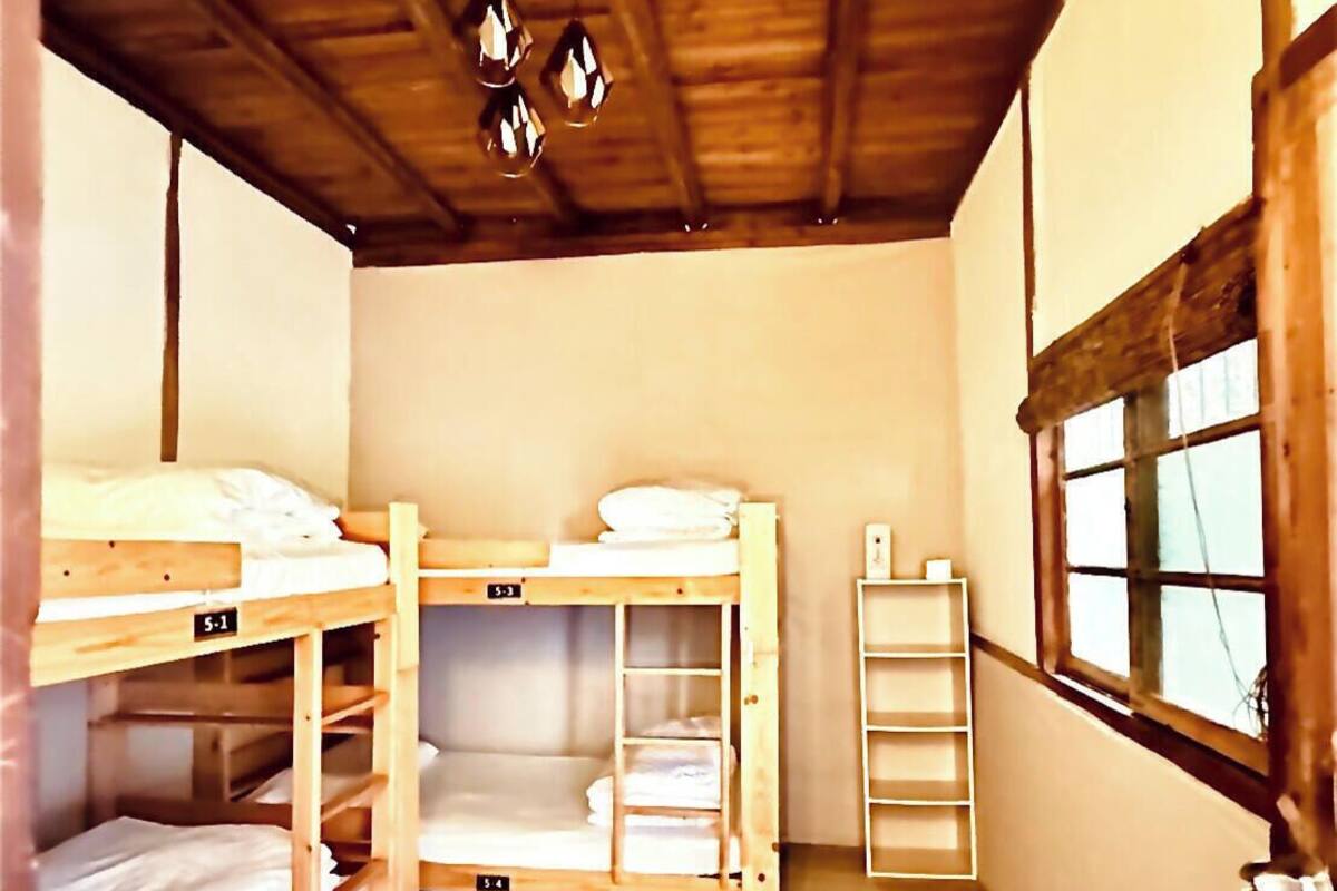 Ein Schlafsaalzimmer mit Etagenbetten, Holzbalken an der Decke, einem Fenster und einer Leiter.