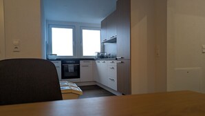 Eine kompakte Küche mit weißen Schränken, einem eingebauten Backofen und einem Fenster über der Spüle.