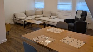 Ein modernes Wohnzimmer mit einer Sofagarnitur, einem Esstisch mit Stühlen und einem schwarzen Bürostuhl.