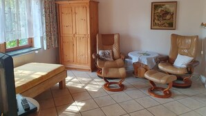 A room with a bed, two rocking chairs, a wooden cabinet, and a painting on the wall.