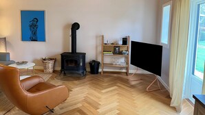 Una sala de estar con un estufa de leña negra, un sillón de cuero marrón, un televisor y una estantería con libros y adornos.