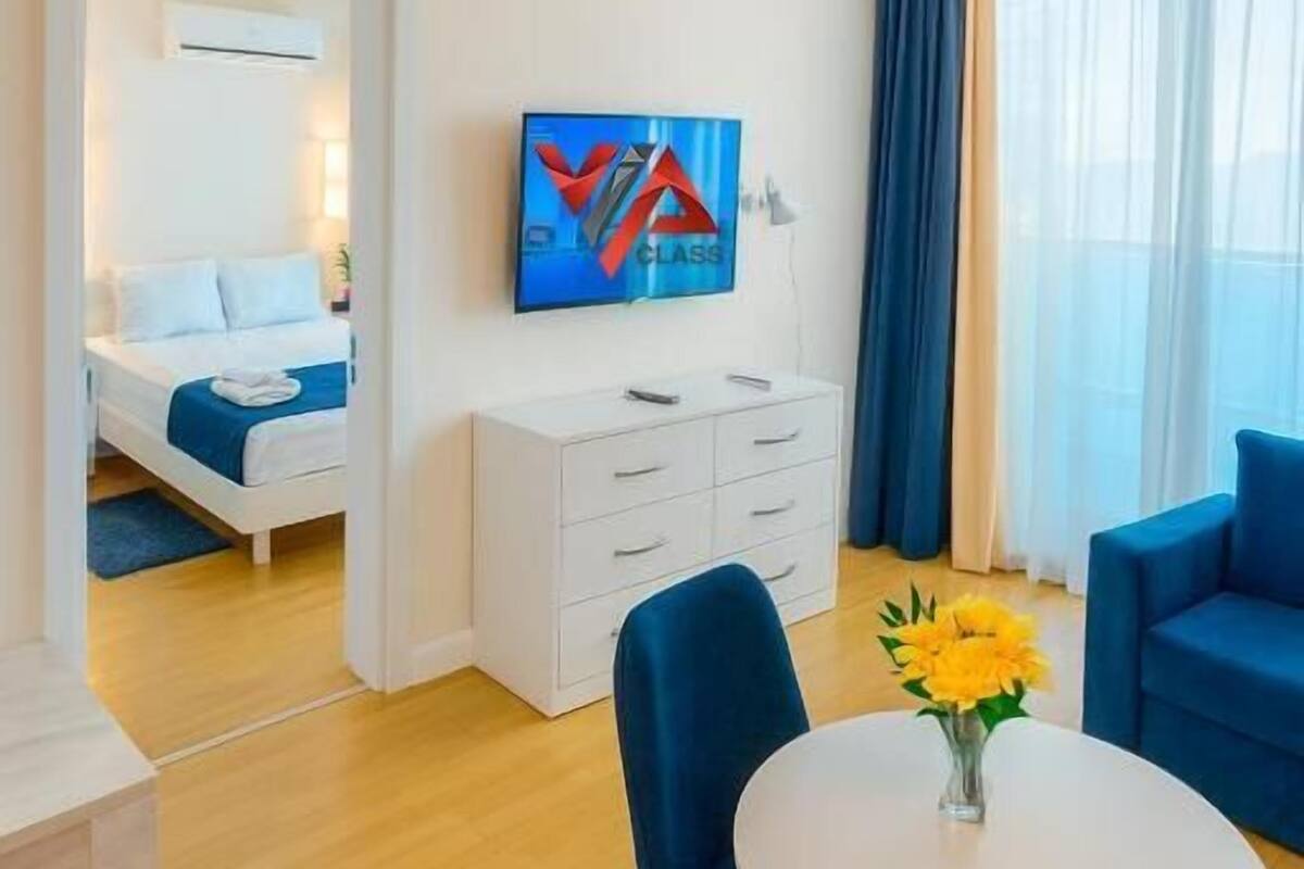 Habitación de hotel con cama, escritorio, silla, mesa con un florero y televisor en la pared.