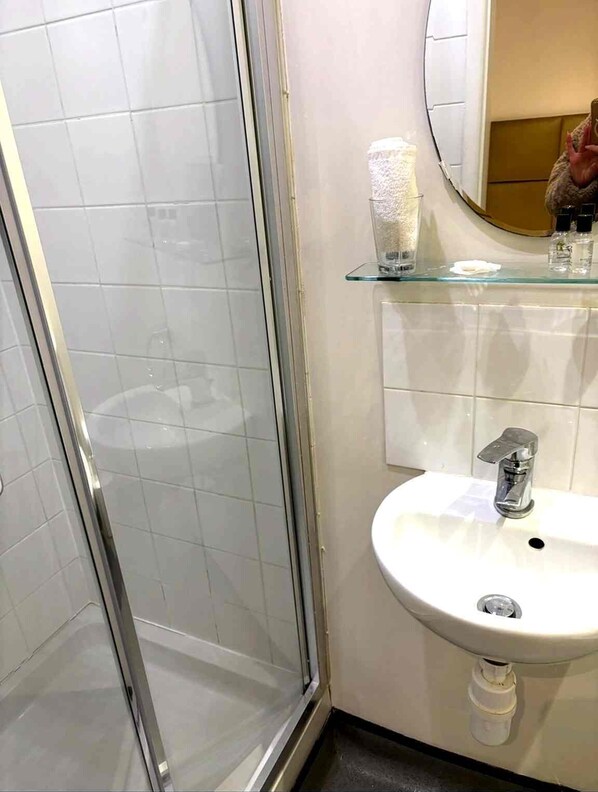 A bathroom with a glass shower enclosure, a sink with a mirror above it, and toiletries on the sink's edge.