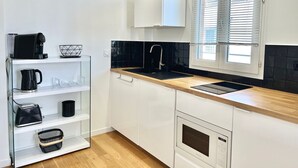 A modern kitchen with white cabinets, a black countertop, a built-in oven, and a window with blinds. - Superb Studio teletravail - Rooftop Paris (Saint-Ouen-sur-Seine)
