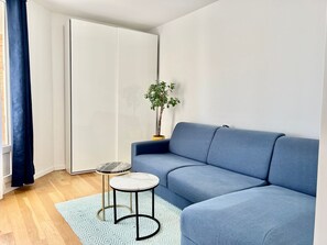 Un salon moderne avec un canapé bleu, une petite table ronde surmontée d’un plateau en marbre, une plante en pot et un placard à portes coulissantes.