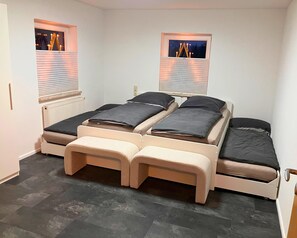 A small, well-lit room with two beds, a bench, and two windows with blinds. - Holiday Apartment De Gruusse (Mildenau)