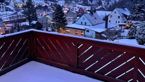 A snow-covered village at dusk with houses and a wooden deck in the foreground. - Holiday Apartment De Gruusse (Mildenau)