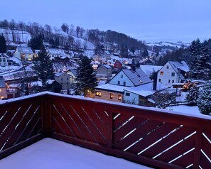 A snow-covered village at dusk with houses and a wooden deck in the foreground. - Holiday Apartment De Gruusse (Mildenau)