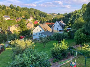 A residential area with houses surrounded by lush greenery and hills in the background. - Holiday Apartment De Gruusse (Mildenau)