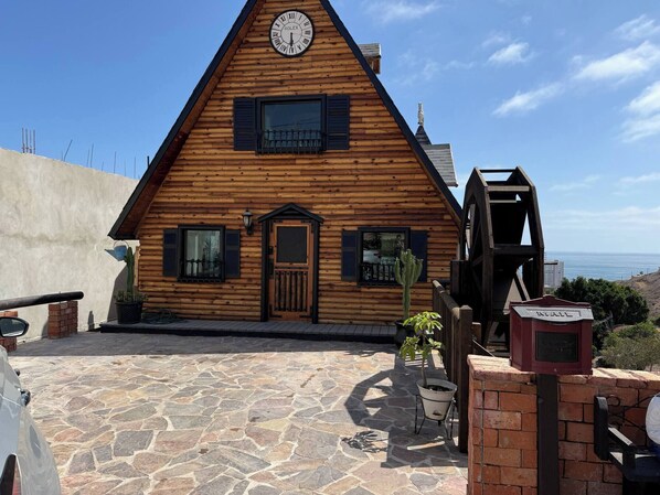 A wooden cabin with a clock, a stone-paved entrance, and a view of the ocean.
